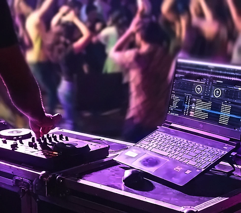 A DJ controller and laptop running mixing software on a road case, with a crowd beyond.